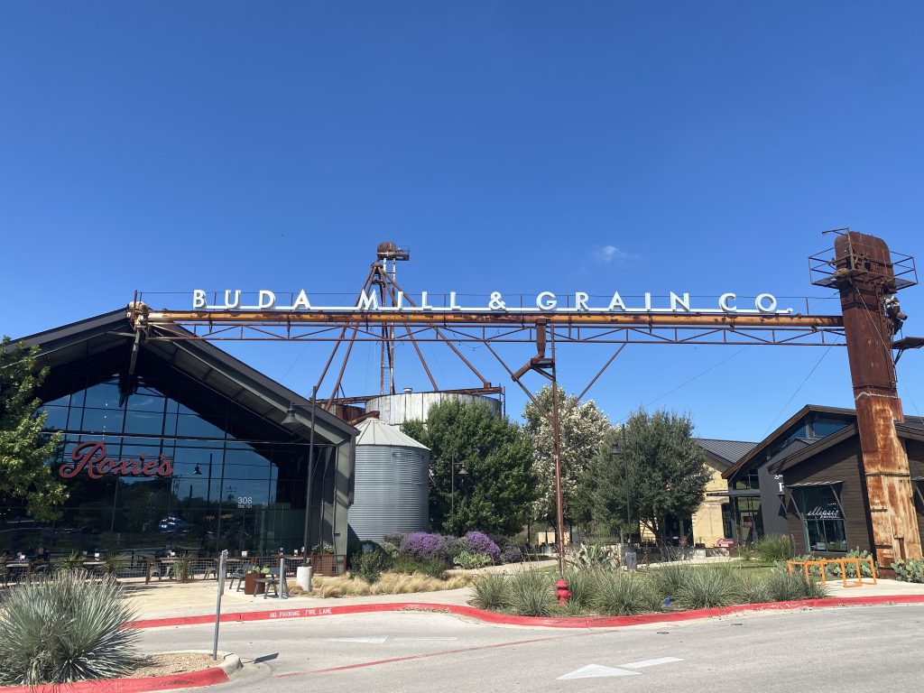 Buda Mill and Grain Co. sign above local shops, restaurants and landscaped walkways.